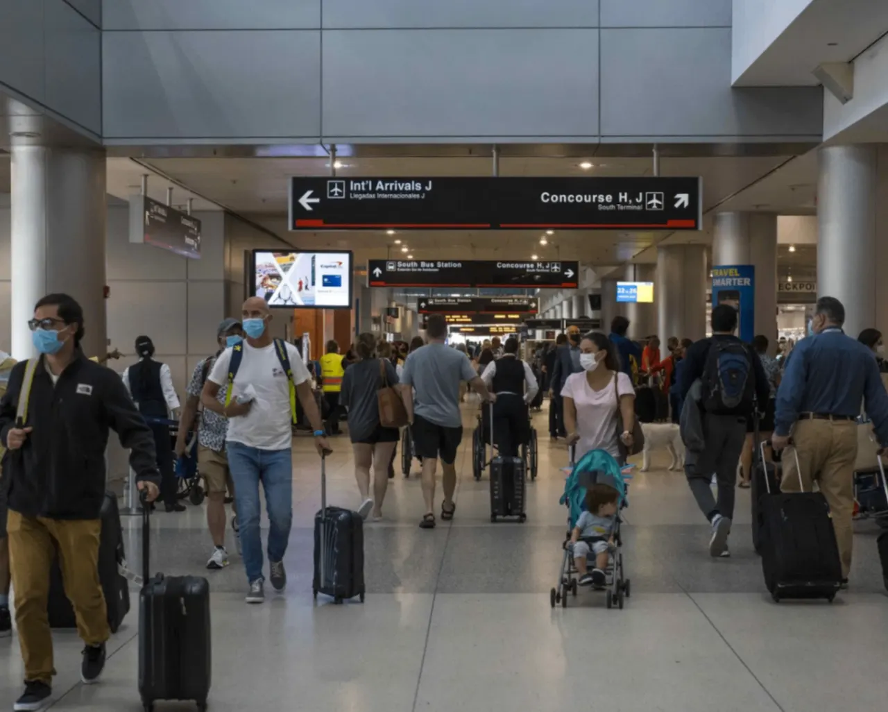 Travelers with luggage walking through Miami International Airport (MIA) arrivals terminal, showcasing the busy airport environment for passengers comparing MIA vs FLL options.