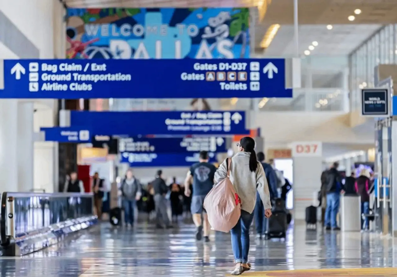 A traveler walking under blue directional signage inside Dallas Fort Worth International Airport, showcasing the terminal environment for passengers deciding between DFW vs DAL.